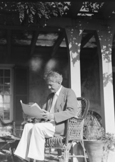Arnold Genthe seated outdoors in a wicker chair reading, between 1911 and 1942. Creator: Arnold Genthe.