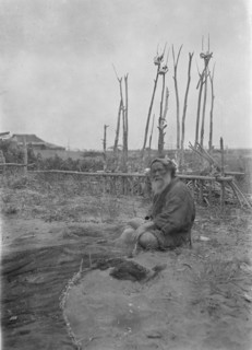 Seated Ainu man working on fishing nets, 1908. Creator: Arnold Genthe.