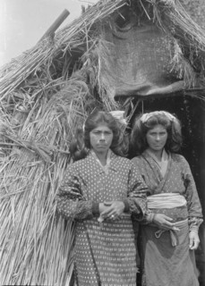 Two Ainu women standing at the entrance of a hut, 1908. Creator: Arnold Genthe.