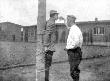 'La peine du poteau; a Zwickau: un Francais, lie au poteau, recoit d'un prisonnier roumain..., 1917. Creator: Unknown.