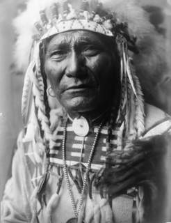 Ghost Bear, Crow Indian, Montana, head-and-shoulders portrait, facing front, feather..., c1908. Creator: Edward Sheriff Curtis.