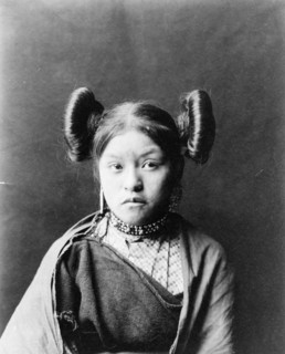 Gobuguoy, Walpi girl, half-length portrait, facing front, hair tied in swirls on sides of..., c1900. Creator: Edward Sheriff Curtis.