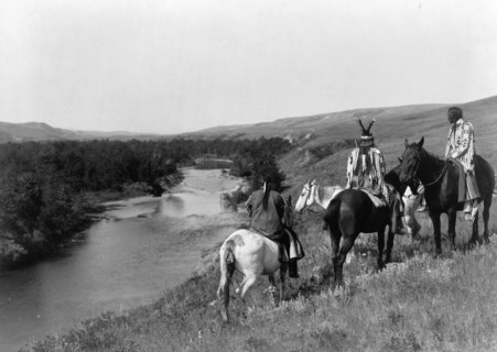Three Piegan Indians and four horses on hill above river, c1910. Creator: Edward Sheriff Curtis.