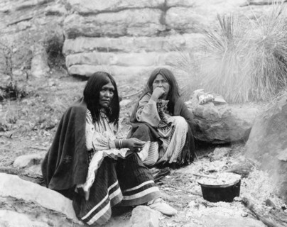 Two Apache Indian women at campfire, cooking pot in front of one, c1903. Creator: Edward Sheriff Curtis.