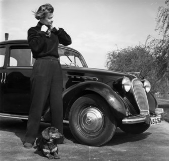 Photographer Kerstin Bernhard stands next to a car with her dachshund, 1955-1960. Creator: Unknown.