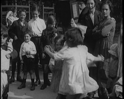 A Group of Civilian Children Dancing in Front of a Hurdy Gurdy Watched by a Small Crowd, 1920. Creator: British Pathe Ltd.