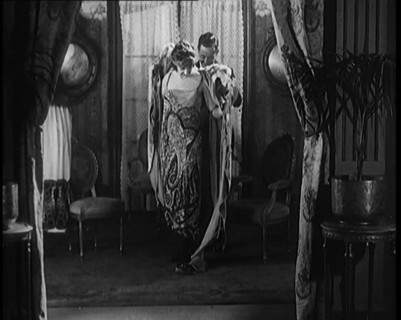 A Male Civilian Helping a Female Civilian Remove Her Fur Coat Revealing an Ornated Gown, 1920. Creator: British Pathe Ltd.