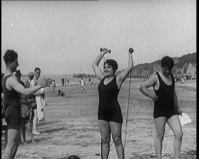 Female Civilian Wearing a Swimsuit Exercising with Elastic Bands on a Beach, 1920. Creator: British Pathe Ltd.