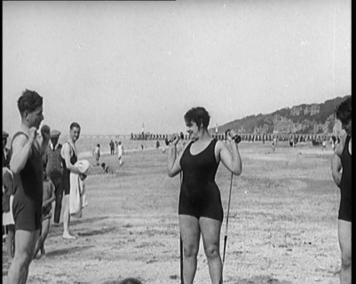 Female Civilian Wearing a Swimsuit Exercising with Elastic Bands on a Beach, 1920. Creator: British Pathe Ltd.