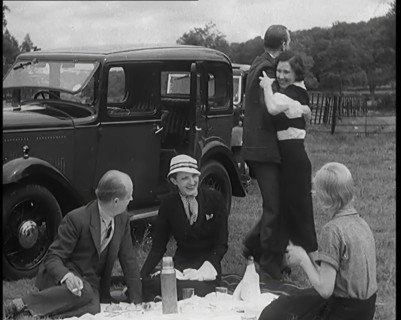 Male and Female Civilians Having a Picnic Beside a Car Whilst Two of Them Are Dancing, 1931. Creator: British Pathe Ltd.