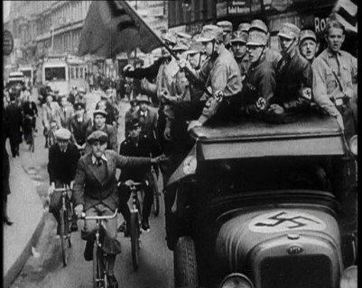 Group of Men in Nazi Uniform Driving Down the Road as Civilians Watch, 1933. Creator: British Pathe Ltd.