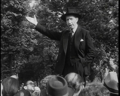 A Close up of a British Man in Dark Suit and Hat Declaiming Before a Crowd from a Raised..., 1938. Creator: British Pathe Ltd.
