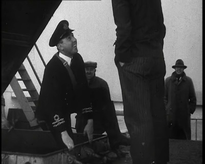 A Male Customs Official Standing by a Hatch and Talking to a Man on Board a Large Ship in..., 1939. Creator: British Pathe Ltd.
