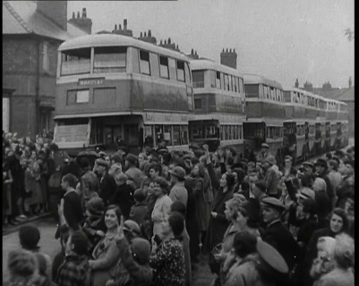 Men, Women, and Children Standing by a Line of Buses Parked in a Residential Street, 1939. Creator: British Pathe Ltd.