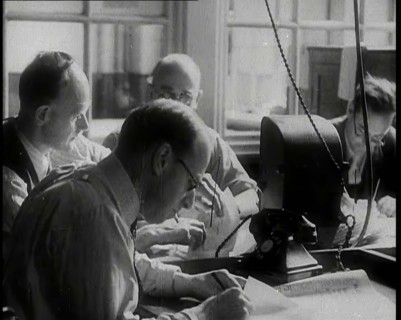 Four Male British Journalists Sitting Around a Table Covered in Papers and Writing, 1939. Creator: British Pathe Ltd.