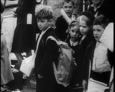 British Child Evacuees Standing on a Pavement With Bags and Boxes as Adults are Standing..., 1939. Creator: British Pathe Ltd.