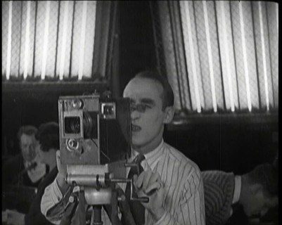 A Male Cameraman Films a Scene Whilst Lights Illuminate Behind Him, 1920s. Creator: British Pathe Ltd.
