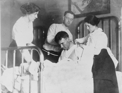 Dr. James F Grant, ship's surgeon, fixing up Gordan G Davidson, survivor of EMPRESS OF..., 1914. Creator: Bain News Service.
