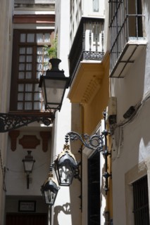 Narrow street with old lamps and balconies in the pedestrian area of Seville, Spain, 2023. Creator: Ethel Davies.