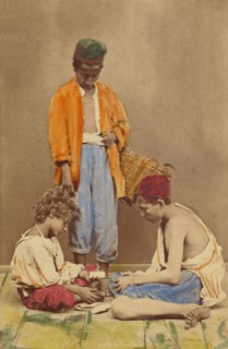 Unidentified man with basket standing, plus two boys seated playing cards, 1865-1870. Creator: Giorgio Conrad.