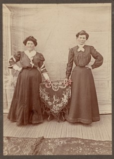 Two women standing at a table holding flowers, about 1875. Creator: Unknown.