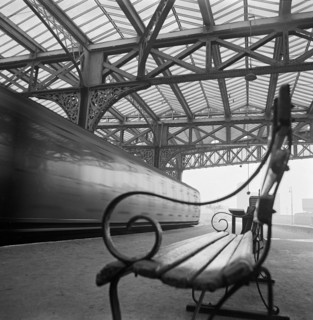 Looking along a bench with curved wrought iron arms on a platform at Waterloo Station with a train