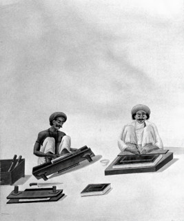 Two Indian bookbinders: one trimming page edges in a press, the other decorating a binding. Creator: Unknown.
