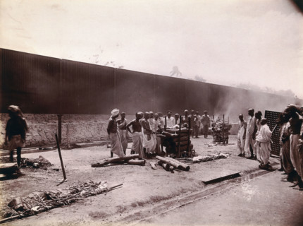 A group of men stand around the body of a man laid out on a pyre of logs during a Hindu...,  1896/97 Creator: Unknown.