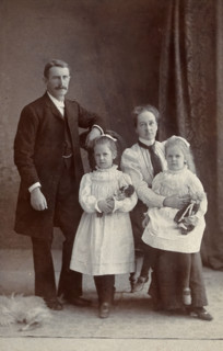 Unidentified family with two girls holding dolls. Creator: Priyalalls Photography.