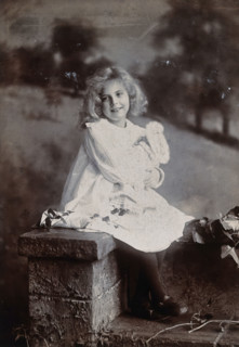 A girl, holding a doll, sitting on a wall, c1890s. Creator: Lock & Whitfield.