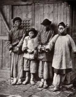 Foochow, China: four people with leprosy, wearing thick clothing, standing outside a wooden..., 1873 Creator: John Thomson.