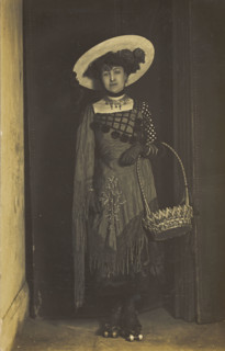 A person wearing a dress, large hat and roller skates, poses holding a basket, (1910-1919?). Creator: Unknown.