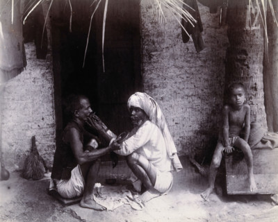 Two Indian men crouching; one is cutting the other's hair, while a girl sits.., c1890s.  Creator: Unknown.