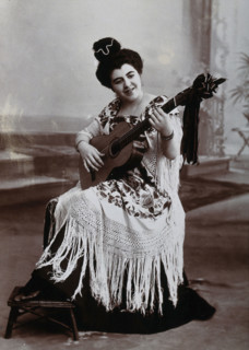 A seated woman, playing a guitar, wearing a fringed shawl, c1900. Creator: Unknown.