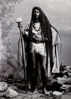 An Indian man with long hair, carrying a staff, in a studio setting, 1900. Creator: Unknown.