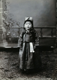 A child posing in front of a painted backdrop in a photographic studio, c1900. Creator: Unknown.