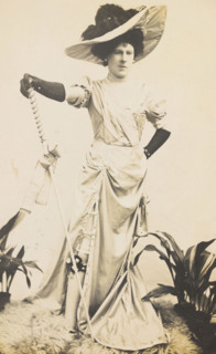 An man in drag is wearing a revealing dress and holding a staff, posing with his..., 1909. Creator: Unknown.