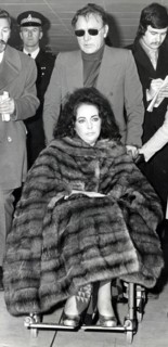 Elizabeth TAYLOR in a wheelchair with Richard BURTON, 1973