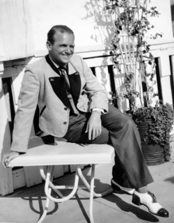 Douglas FAIRBANKS Jr., seated on a table