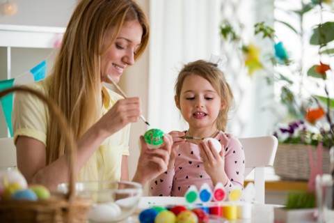 A mother and daughter celebrating Easter, painting eggs with brush. Cute little girl in bunny ears preparing the holiday.
