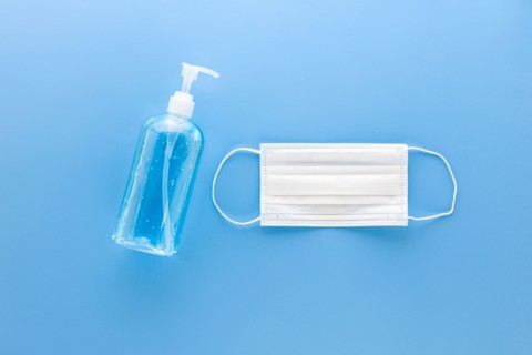 White medical mask and alcohol hand gel sanitizer to protect from virus and grem top view on blue background