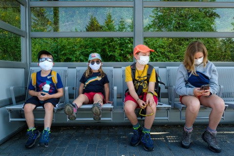 Aha, Baden-Württemberg, Germany - July 28 2020 : 4 children (between 5 and 12 years old), sitting on a bench waiting for a train, wearing face masks.