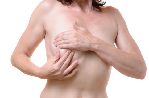 Naked middle-aged woman checking her breast for lumps as a precursor to cancer palpating the tissue between her fingers, close u