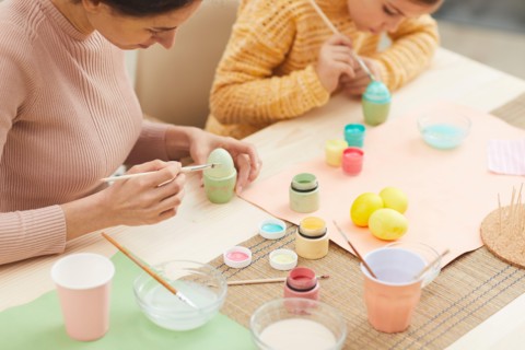 High angle portrait of mother and daughter painting Easter eggs pastel colors sitting at table in cozy kitchen interior, copy space