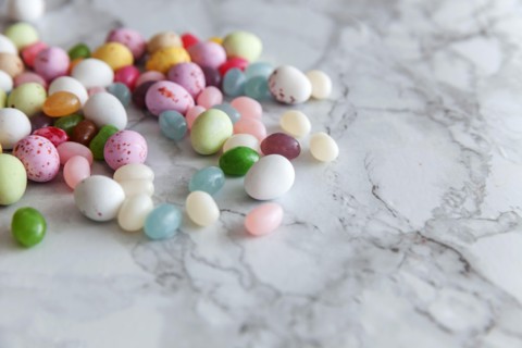 Happy Easter concept. Preparation for holiday. Easter candy chocolate eggs and jellybean sweets on trendy gray marble background. Simple minimalism fl