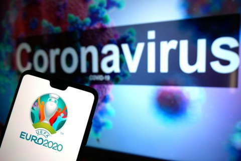 The UEFA Euro 2020 logo seen displayed on a mobile phone with an illustrative model of the Coronavirus displayed on a monitor in the background.