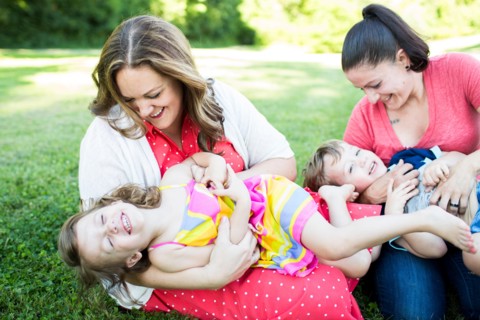 Playful lesbian mothers playing, tickling children in grass
