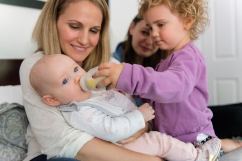 Caucasian girl feeding bottle to baby sister