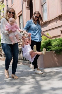 Caucasian mothers swinging daughter on city sidewalk