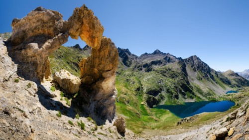 The Arc de Tortisse, famous natural limestone arch in the national park of Mercantour (France) with the upper lake of Vens on the background